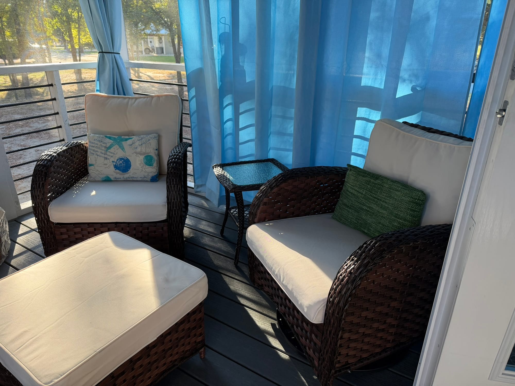 Woven swivel rocking chairs with ottomans on screened porch of tiny house with view of trees
